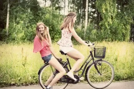 Two young women riding a bicycle together on a forest path in Sweden.