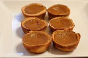 Six mini pumpkin pie tarts arranged on a white plate