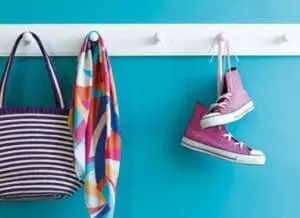Colorful striped tote bag, patterned scarf, and pink sneakers hanging on turquoise wall hooks.