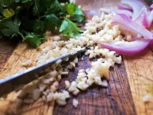 Minced garlic on a cutting board with fresh cilantro and sliced red onion