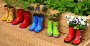 Children's rain boots repurposed as planters with flowers and herbs on wooden deck