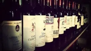 Row of French wine bottles with white labels displayed against dark bottles in background