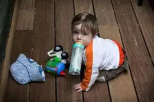 Toddler on wooden floor with toy truck and water bottle