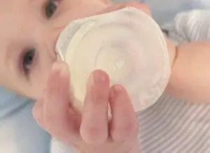 Baby holding a clear plastic container with liquid residue