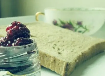 Jar of berries next to whole grain toast with spread and herbal tea