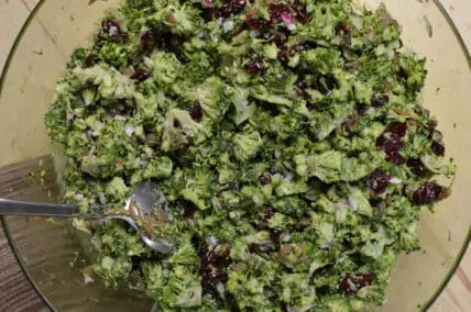 Broccoli salad with dried cranberries in a glass bowl with serving spoon