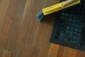 Paintbrush with yellow handle cleaning wooden floor near air vent