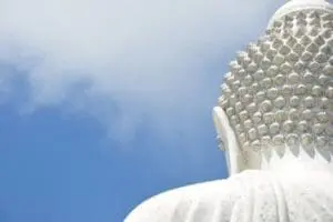 Close-up of a white Buddha statue's face and shoulder against blue sky