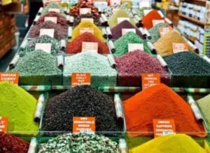 Colorful bulk spices displayed in bins at a market with orange label tags