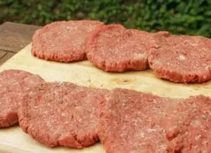 Raw ground beef patties on a wooden cutting board