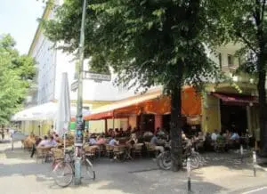 Outdoor café with orange awning and diners seated at tables under trees