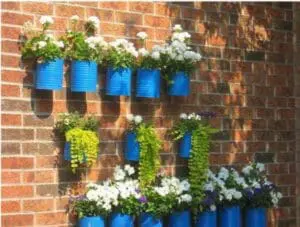 Blue tin cans with white and purple flowers mounted on a brick wall
