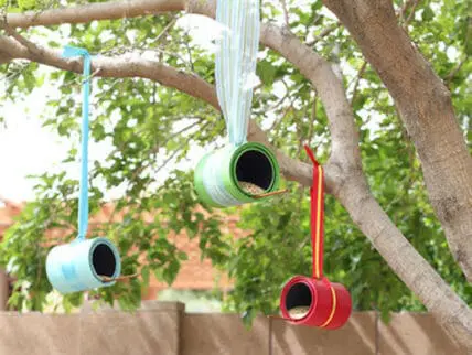Hanging painted tin can bird feeders suspended from tree branches