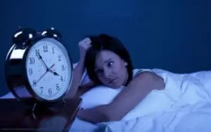 Woman in bed looking at alarm clock showing 3 o'clock at night