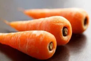 Three peeled carrots with their cores visible on a dark surface