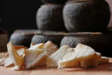 Sliced aged cheese with wheels blurred in background on wooden surface