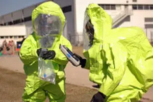 Two people in bright yellow hazmat suits and respirators examining a container during a chemical
