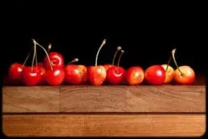 Fresh red cherries arranged on a wooden board against a black background
