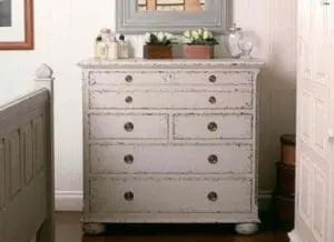 Distressed white painted dresser with mirror and decorative items on top in bedroom setting