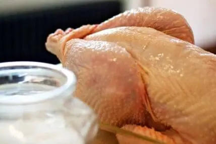 Raw chicken being rinsed under running water in a kitchen sink