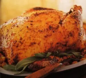 Golden-brown roasted organic chicken garnished with fresh sage on a plate