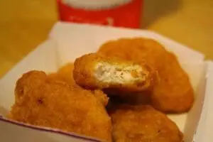 Golden-brown fried chicken nuggets on a white paper container with one cut in half showing the
