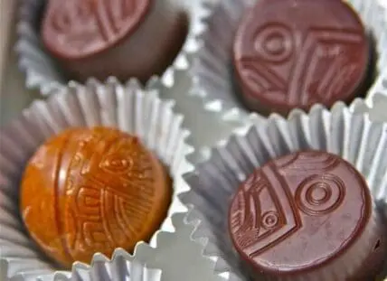 Four chocolate truffles with decorative patterns in white candy cups