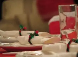 Festive table setting with red and white napkins decorated with small holly sprigs