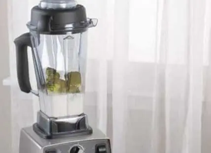 Vitamix blender with green smoothie ingredients in clear pitcher on base unit