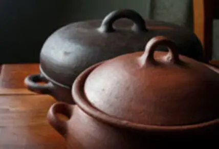 Two rustic clay cooking pots with lids on a wooden table.