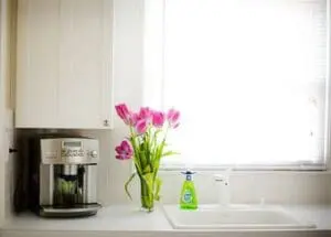Clean kitchen countertop with coffee maker, fresh pink tulips, and dish soap by window