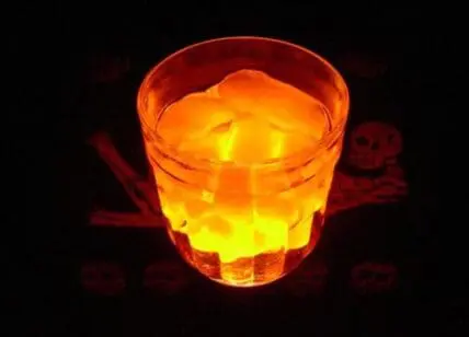 Glowing orange and yellow Halloween cocktail in a rocks glass against a dark background with skull