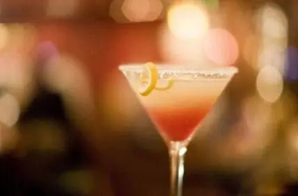 A cocktail with red liquid, sugared rim, and lemon twist in a martini glass.
