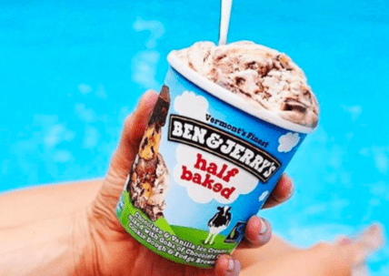 Hand holding Ben & Jerry's Half Baked ice cream cone against blue sky background