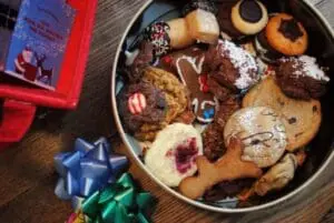 Assorted holiday cookies and treats in a decorative tin with gift bows