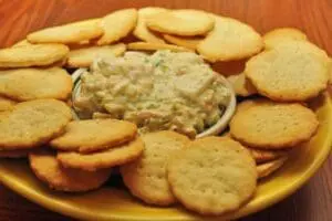 Crackers arranged around a bowl of creamy dip on a yellow plate
