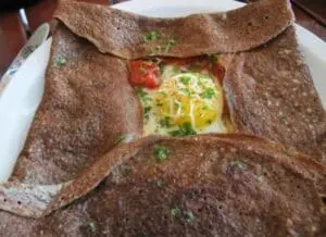 Buckwheat crepe with egg, cheese, and tomato filling on white plate