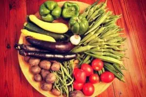 Fresh organic vegetables arranged on a wooden board including eggplants, squash, green beans