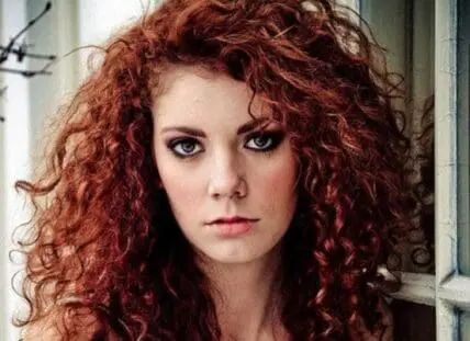 Woman with voluminous red curly hair looking at camera