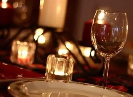 Romantic candlelit dinner table setting for two with wine glass and plated dinnerware