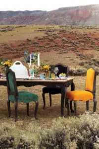 Elegant outdoor dining setup with colorful chairs and flowers in an arid landscape.