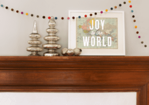 Mantelpiece decorated with gold Christmas trees, ornaments, and a "Joy to the World" framed print