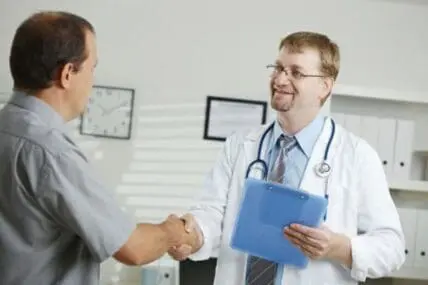 Doctor shaking hands with patient in medical office while holding clipboard