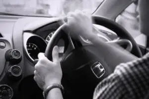 Person gripping steering wheel while driving car interior in black and white