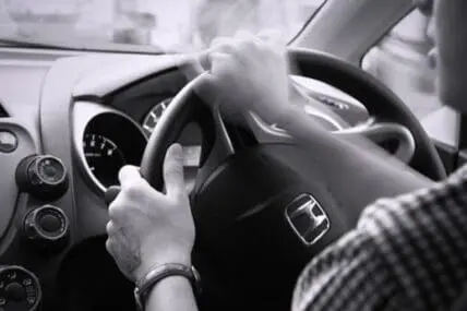 Person gripping steering wheel while driving car interior in black and white