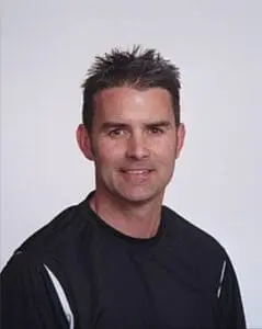 Professional headshot of a man in a black athletic shirt against a white background