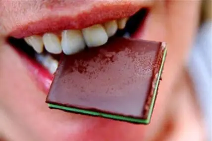 Close-up of a person biting into a square of dark chocolate