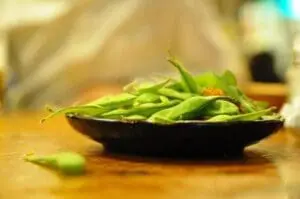 Fresh edamame beans in a black bowl on a wooden surface