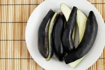 Sliced eggplants with dark purple skin and pale green flesh on a white plate