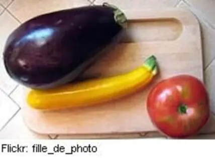 Fresh eggplant, yellow pepper, and tomato on a wooden cutting board